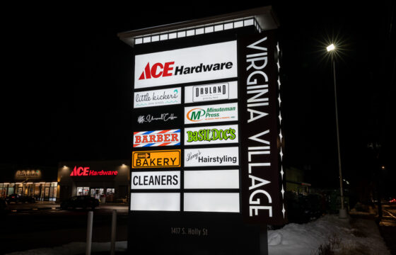 Illuminated Virginia Village monument sign at night with glowing push-through letters and backlit tenant panels.